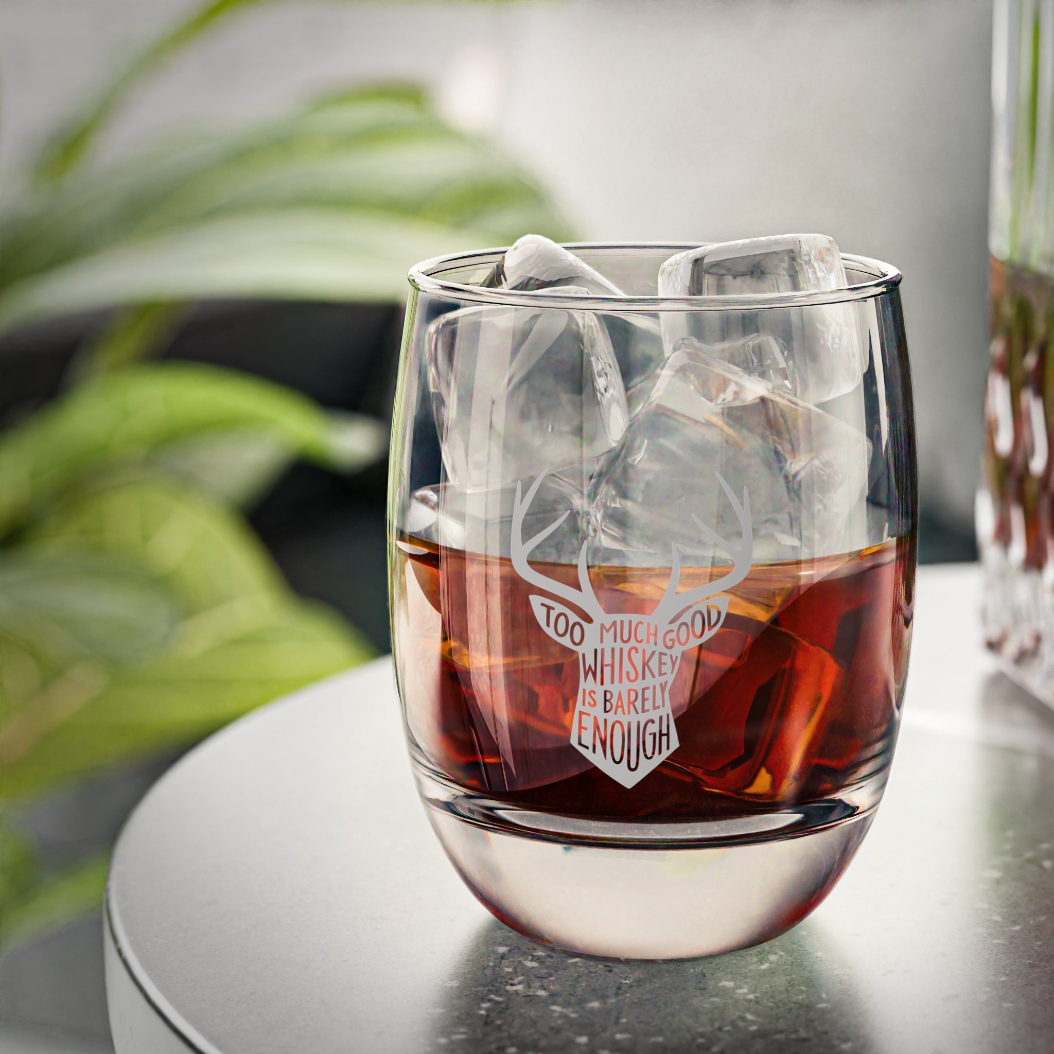 Whiskey glass with engraved quote and ice cubes on a modern table
